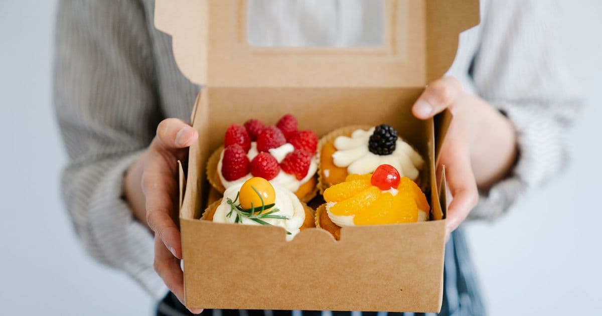 Close-up of a woman holding a box filled with assorted fresh fruit cupcakes, perfect for dessert.