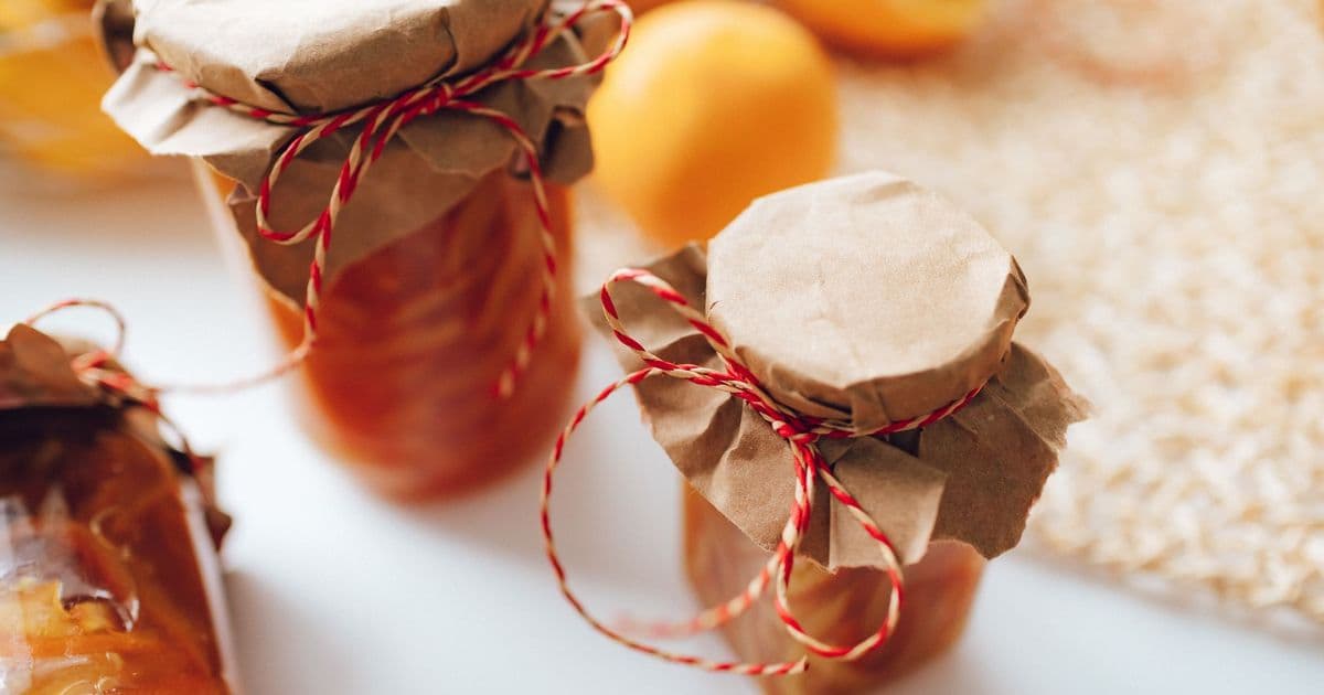 A close-up image of homemade preserves in jars wrapped with paper and string, indoors.
