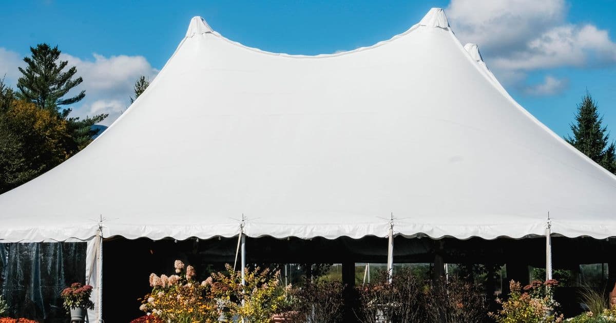 A sleek white tent set up outdoors under a vibrant blue sky with fluffy clouds.