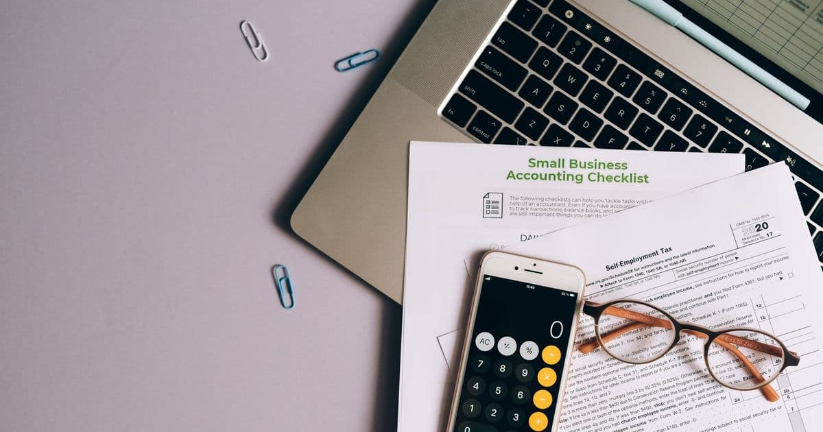 Flat lay of small business accounting tools including tax form, phone, and glasses on a desk.