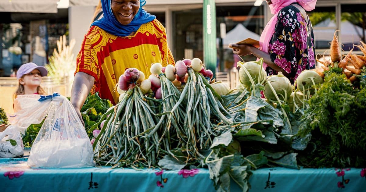 Two women engage in friendly commerce at a colorful outdoor vegetable market.