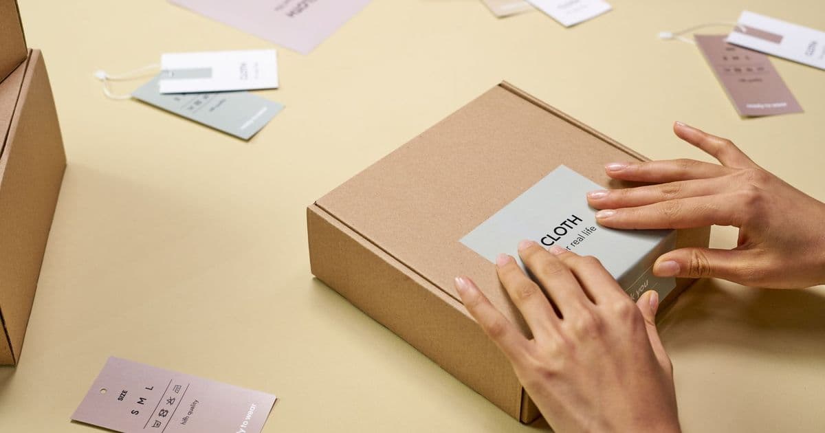 Hands carefully packing a cardboard box with multiple tags around, emphasizing sustainable packaging.