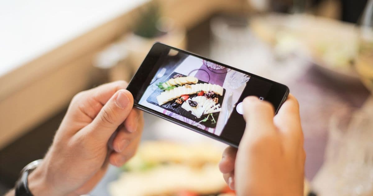 Hands holding a smartphone capturing a photo of a plated dish in a cozy setting.