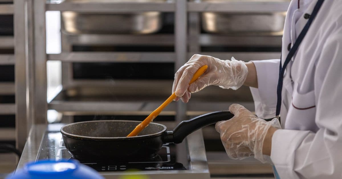 Chef in professional kitchen cooking with frying pan using stovetop.